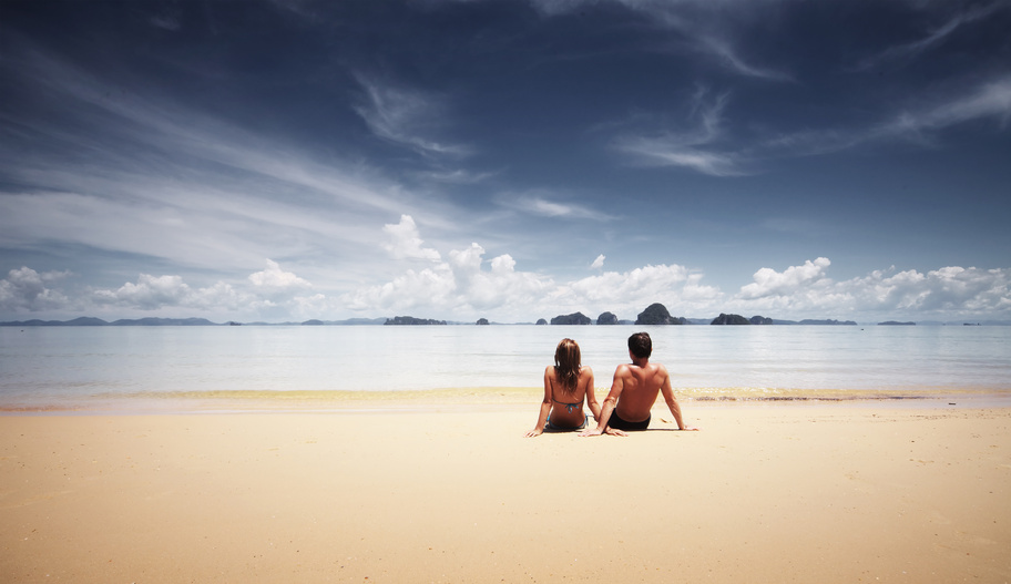 Young couple sitting on a sand and looking to a sea